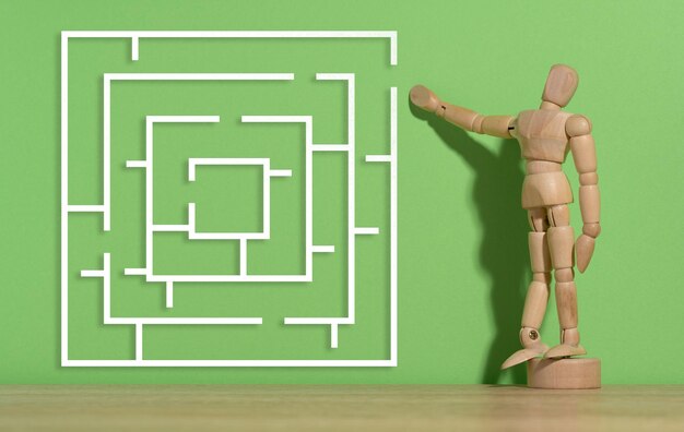 Wooden figurine of a mannequin and a labyrinth on a green background Solution search concept