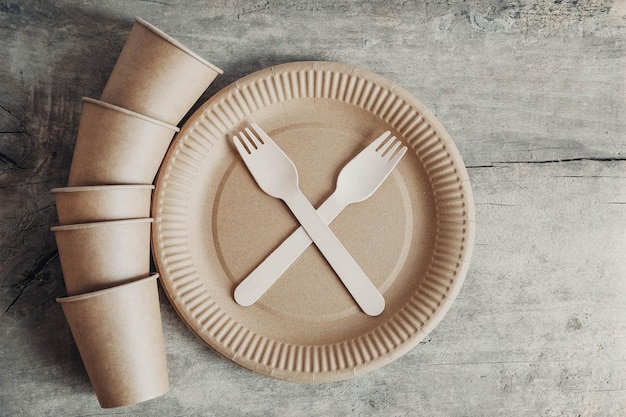 Wooden forks and paper cups with plates on wooden background Eco friendly disposable tableware