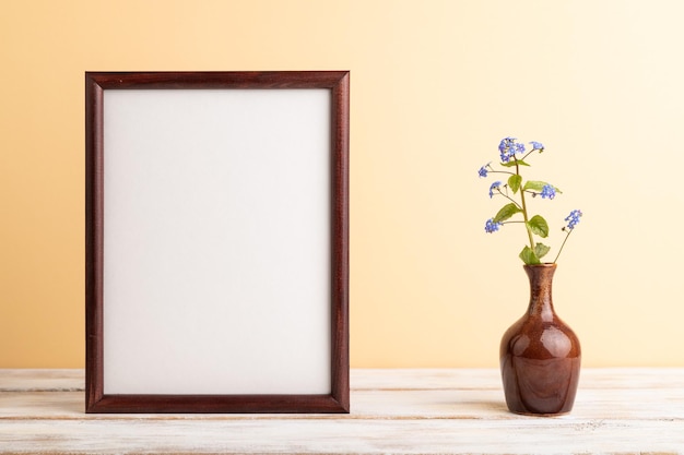 Wooden frame with blue forgetmenot flowers in ceramic vase on orange pastel background side view copy space mockup