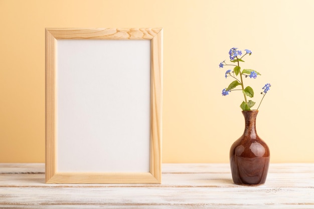 Wooden frame with blue forgetmenot flowers in ceramic vase on orange pastel background side view copy space mockup