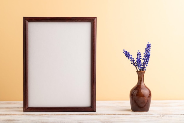 Wooden frame with blue muscari hyacinth flowers in ceramic vase on orange pastel background side view copy space mockup