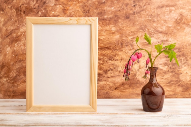 Wooden frame with pink dicentra broken heart in ceramic vase on brown concrete background side view copy space