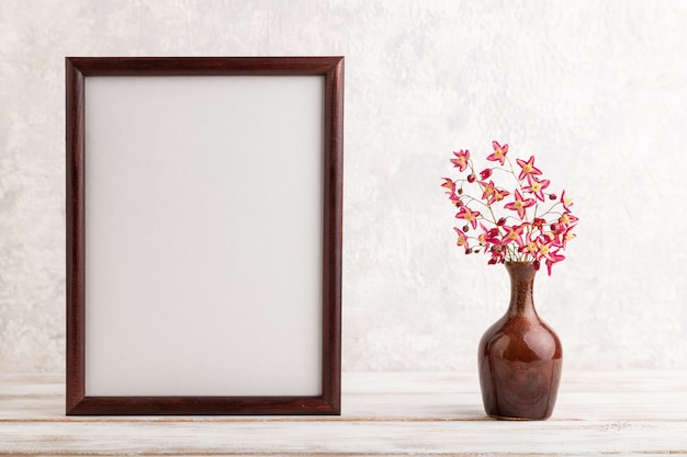 wooden frame with purple barrenwort flowers in ceramic vase on gray concrete background. copy space