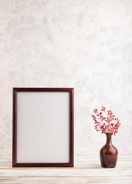 Wooden frame with purple barrenwort flowers in ceramic vase on gray concrete background side view copy space mockup