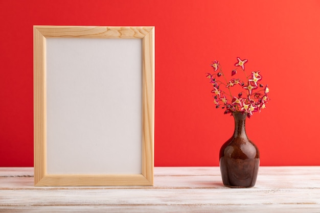 wooden frame with purple barrenwort flowers in ceramic vase on red pastel background.  copy space