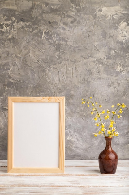 Wooden frame with yellow barrenwort flowers in ceramic vase on gray concrete background side view copy space mockup