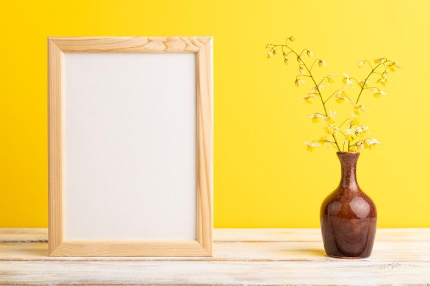 Wooden frame with yellow barrenwort flowers in ceramic vase on yellow pastel background side view copy space mockup