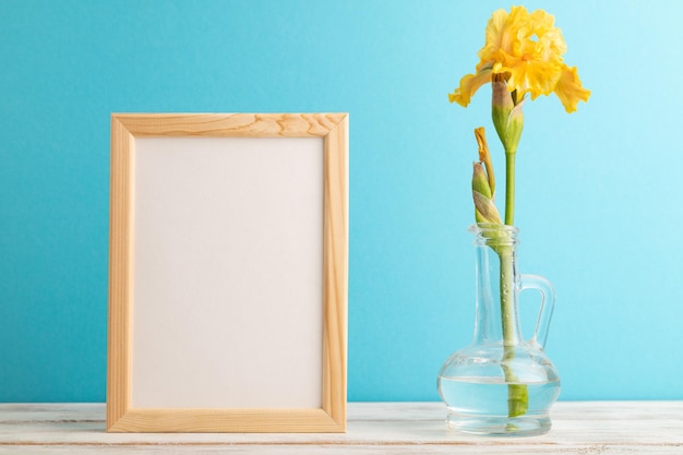 Wooden frame with yellow iris flower in glass on blue pastel background side view copy space