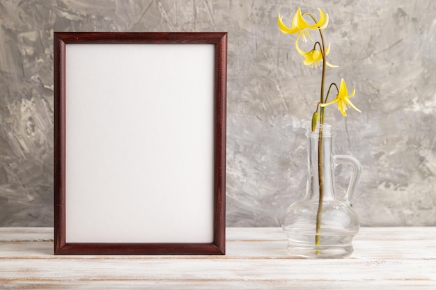 Wooden frame with yellow trout lily or dogtooth violet flowers in glass on gray concrete background side view copy space mockup