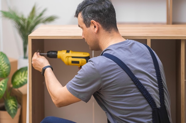 Wooden furniture industry man attaching door hinge to wooden cabinet with drilling machine