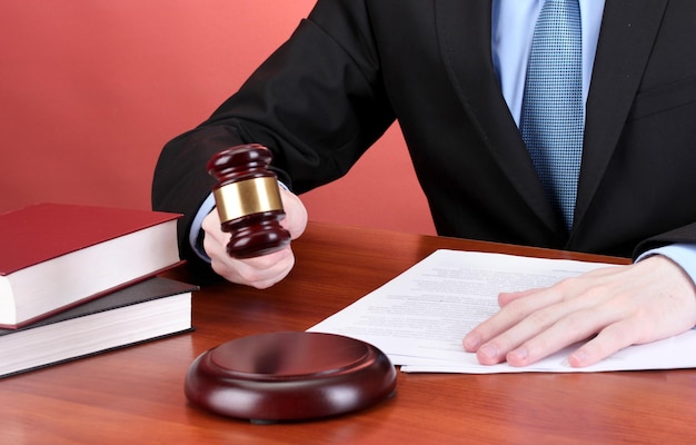 Wooden gavel in hand and books on wooden table on red background