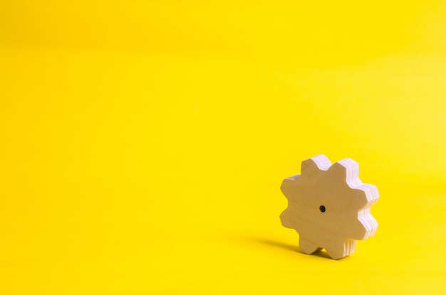 Photo a wooden gear on a yellow background. the concept of technology and business processes.