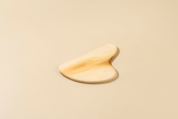 A wooden guasha massager for face lying on a beige background minimalism concept