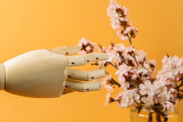 Wooden hand and Beautiful flowering branches in glass jar on orange background