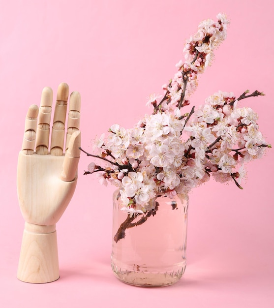 Wooden hand and Beautiful flowering branches in glass jar on a pink background