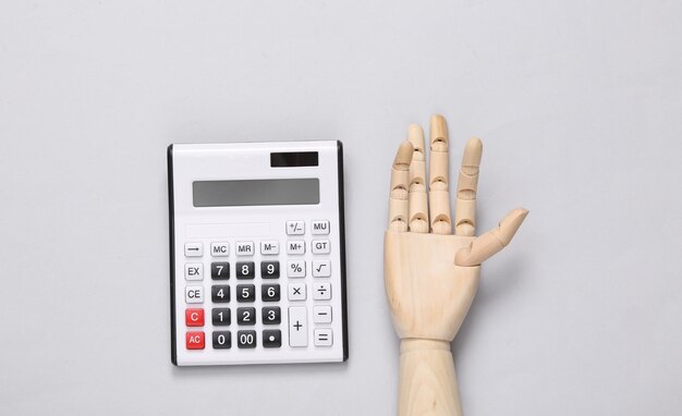 Wooden hand and calculator on gray background Top view