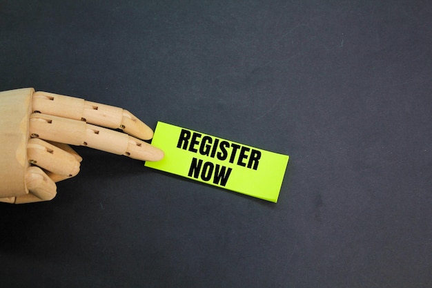 wooden hand and colored paper with the words Register now REGISTER NOW concept