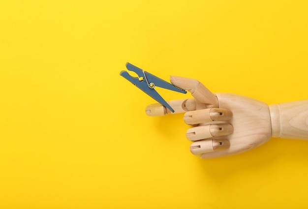 Photo wooden hand holding a clothespin on a yellow background