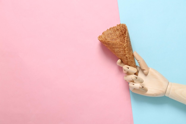 Wooden hand holding Empty waffle cone on pink blue background