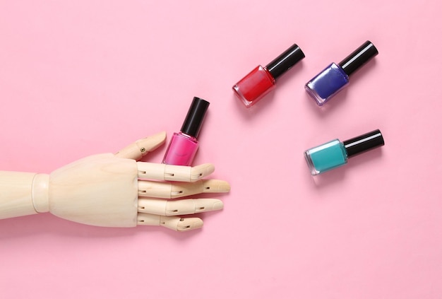 Wooden hand holding nail polish bottles on pink background