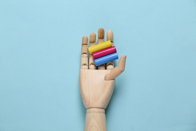 Wooden hand holds colored aa batteries on a blue background