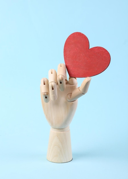 Wooden hand holds heart on blue background