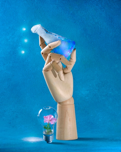 Photo wooden hand holds a laboratory flask with a glowing liquid and a light bulb with a flower inside