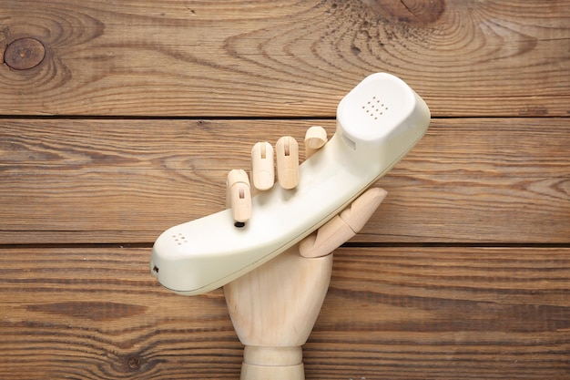 Wooden hand holds phone tube on wooden background