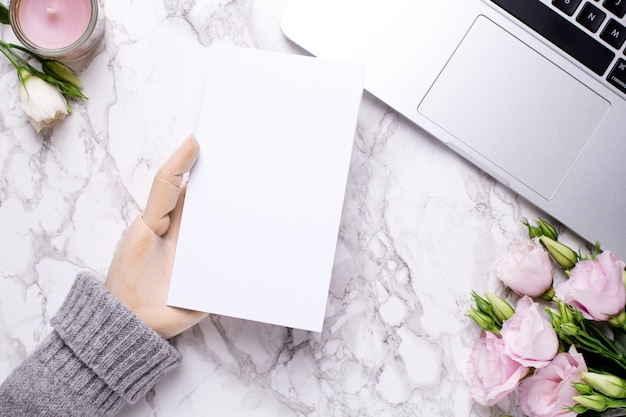 Wooden hand with white present card on marble office table with pink flowers