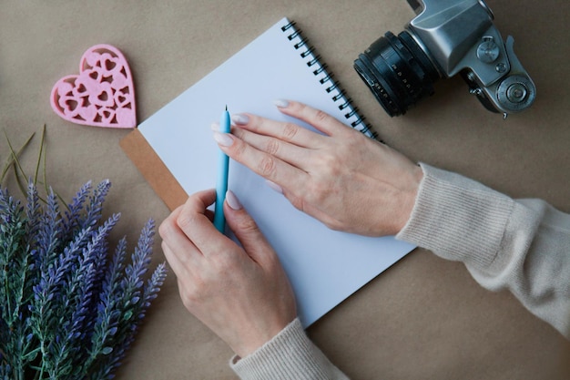 Wooden heart LOVE and woman hands behind notebook on the table and retro camera. Letter writting concept. Heart shape symbol. Valentines - romantic greeting and letters lifestyle feelings concept