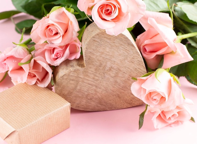 Wooden heart, pink rose flowers and gift box on the pink background