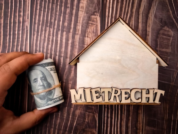 Wooden house and hand holding banknotes with word MIETRECHT on wooden background