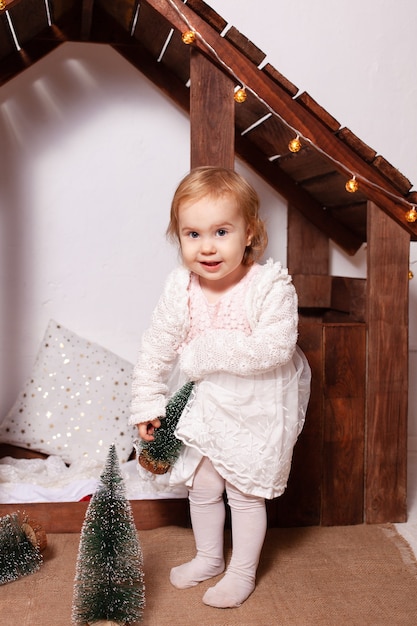 a wooden house. A happy child plays with toys, Artificial little Christmas trees.