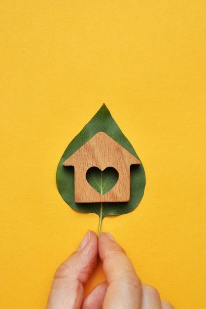 A wooden house on a leaf of a plant in the hands of a man A symbol of environmentally friendly housing