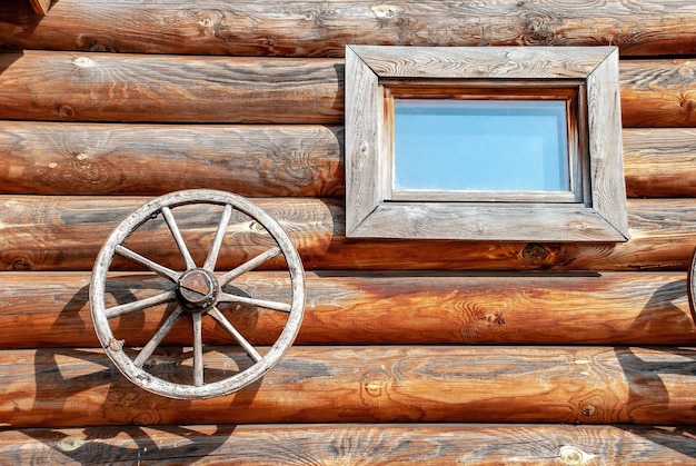 Photo wooden house made of rounded logs with window and two wooden wheels under bright sunlight