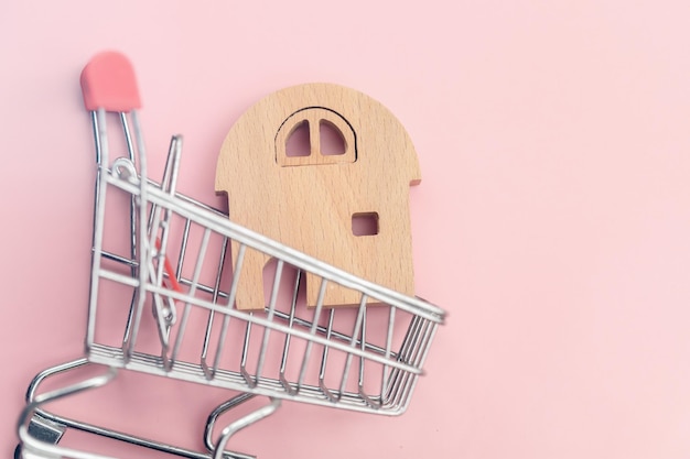 Wooden house model in the shopping cart on pink background for housing and property concept