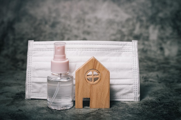 Wooden house model with the bottle of alcohol gel and hygiene face mask on dark background for healthcare selfquarantine and staying home in coronavirus or Covid19 situation concept