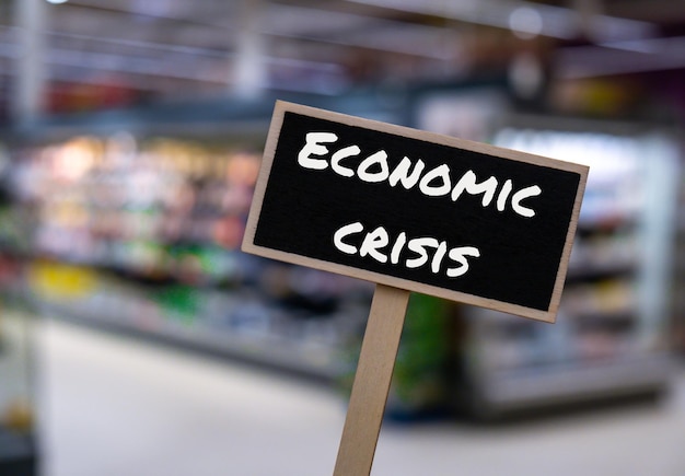 Wooden information label sign with text ECONOMIC CRISIS against defocused store shelves message