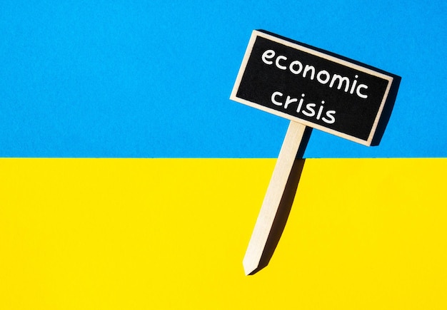 Wooden information label sign with text ECONOMIC CRISIS against Ukrainian national flag message