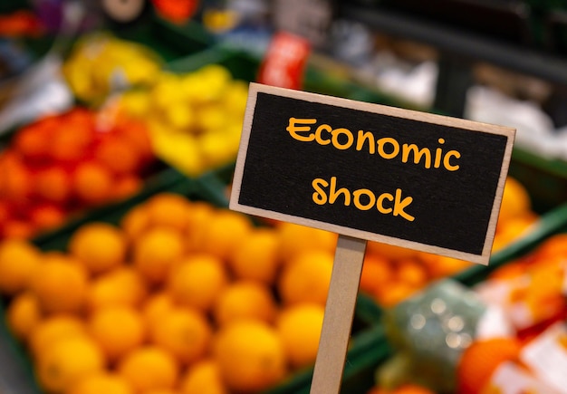 Wooden information label sign with text ECONOMIC SHOCK against defocused store shelves message