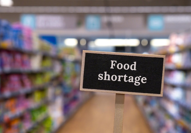 Wooden information label sign with text FOOD SHORTAGE against defocused store shelves