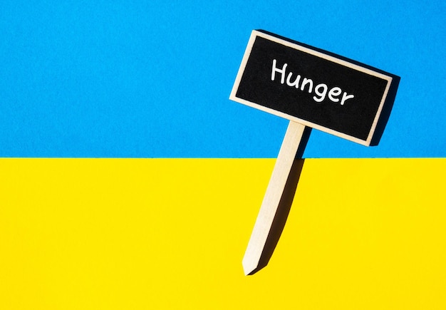 Wooden information label sign with text HUNGER against Ukrainian national flag message Global hunger