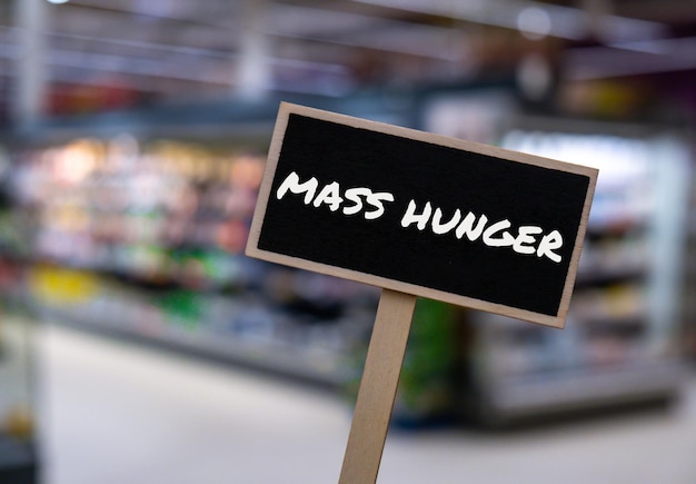 Wooden information label sign with text MASS HUNGER against defocused store shelves message