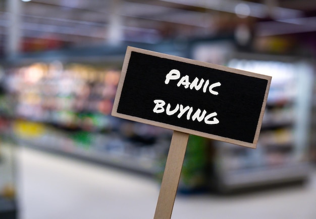 Wooden information label sign with text PANIC BUYING against defocused store shelves message