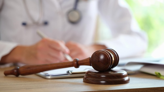 Wooden judge gavel on medical clinic desk and doctor doing paperwork in background legal