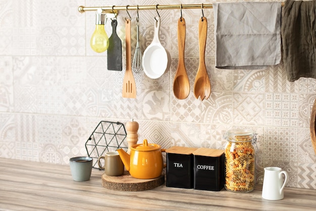 Wooden kitchen utensils hanging on metal railing. Ceramic plates, dishes and cozy decor on table