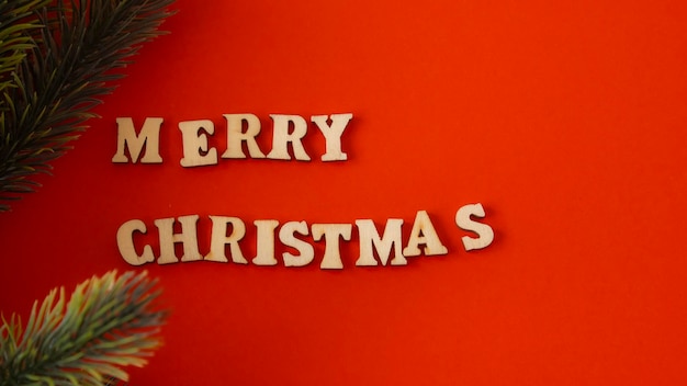 Wooden letters on a deep red background written in English quotMerry Christmasquot next to a green branch of fir