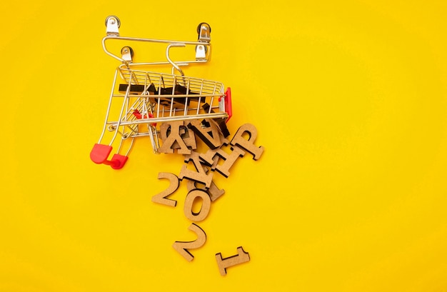 Wooden letters fell from a grocery cart on a yellow background.