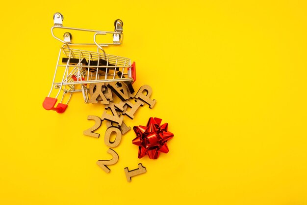 Wooden letters fell out of a grocery cart with a red packing bow on a yellow background.