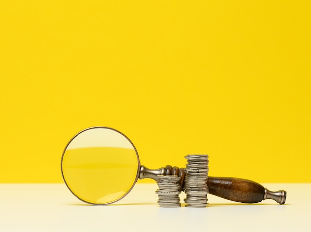 Wooden magnifier and white coins on the table. Income growth concept, high percentage of investment. Search for new sources of income, subsidy